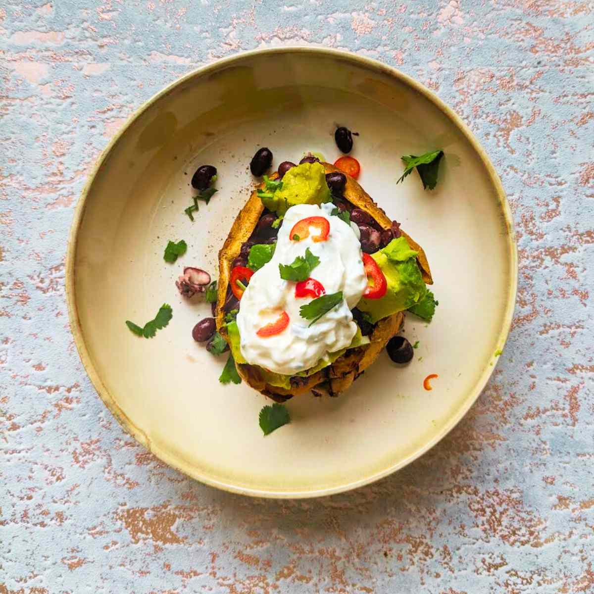 A baked sweet potato with avocado and black bean topping