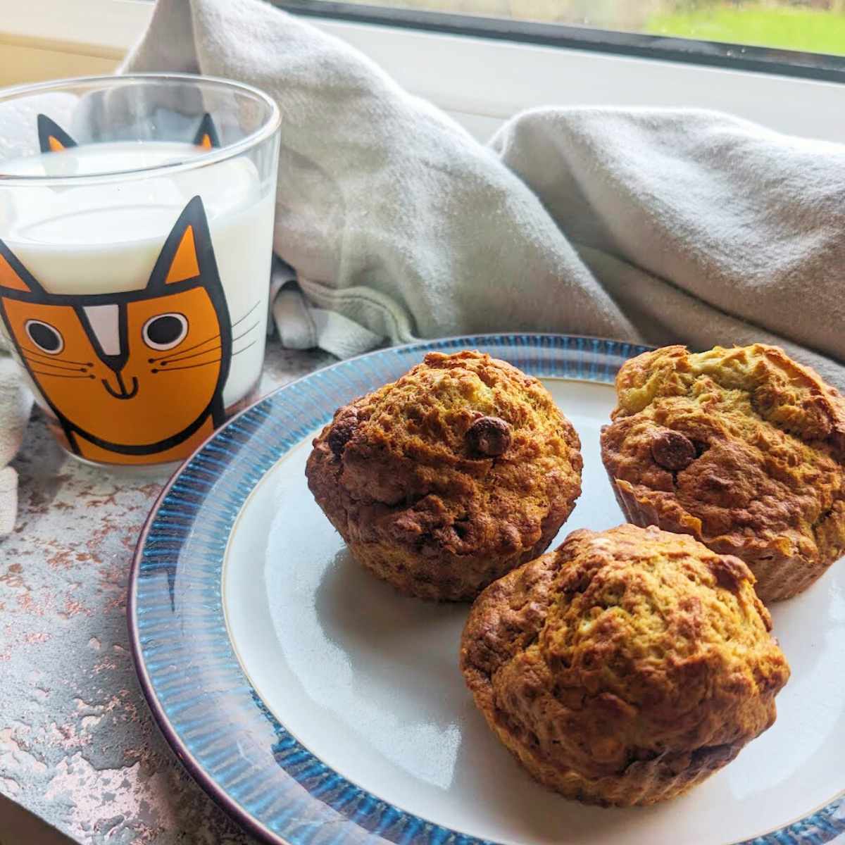 Three banana muffins sit on a plate with a glass of milk besides them.