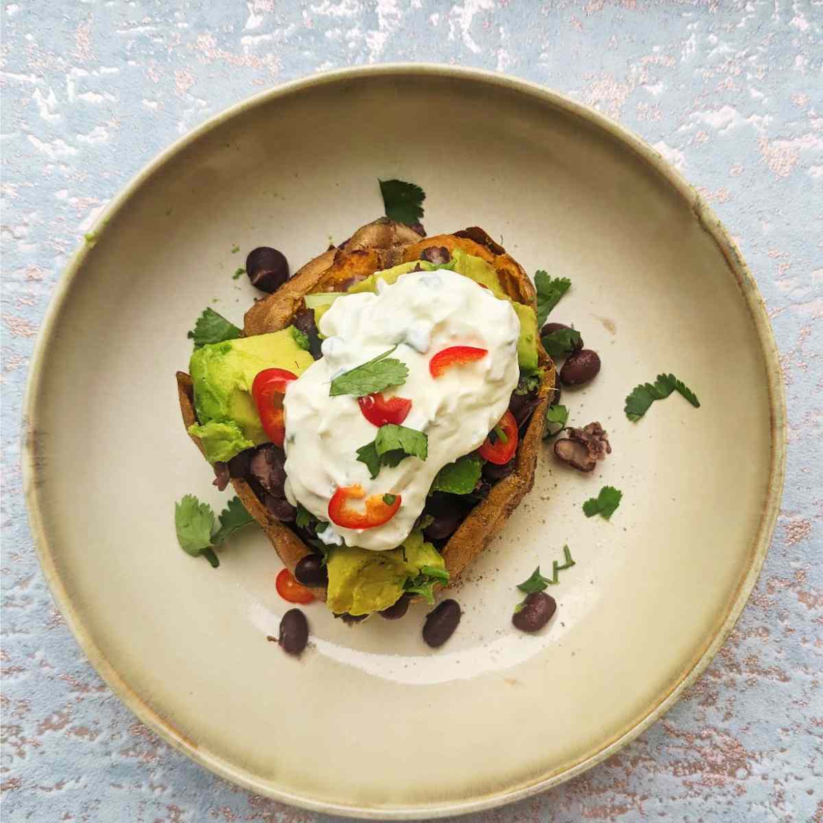 A baked sweet potato with toppings in the center of a cream bowl. 