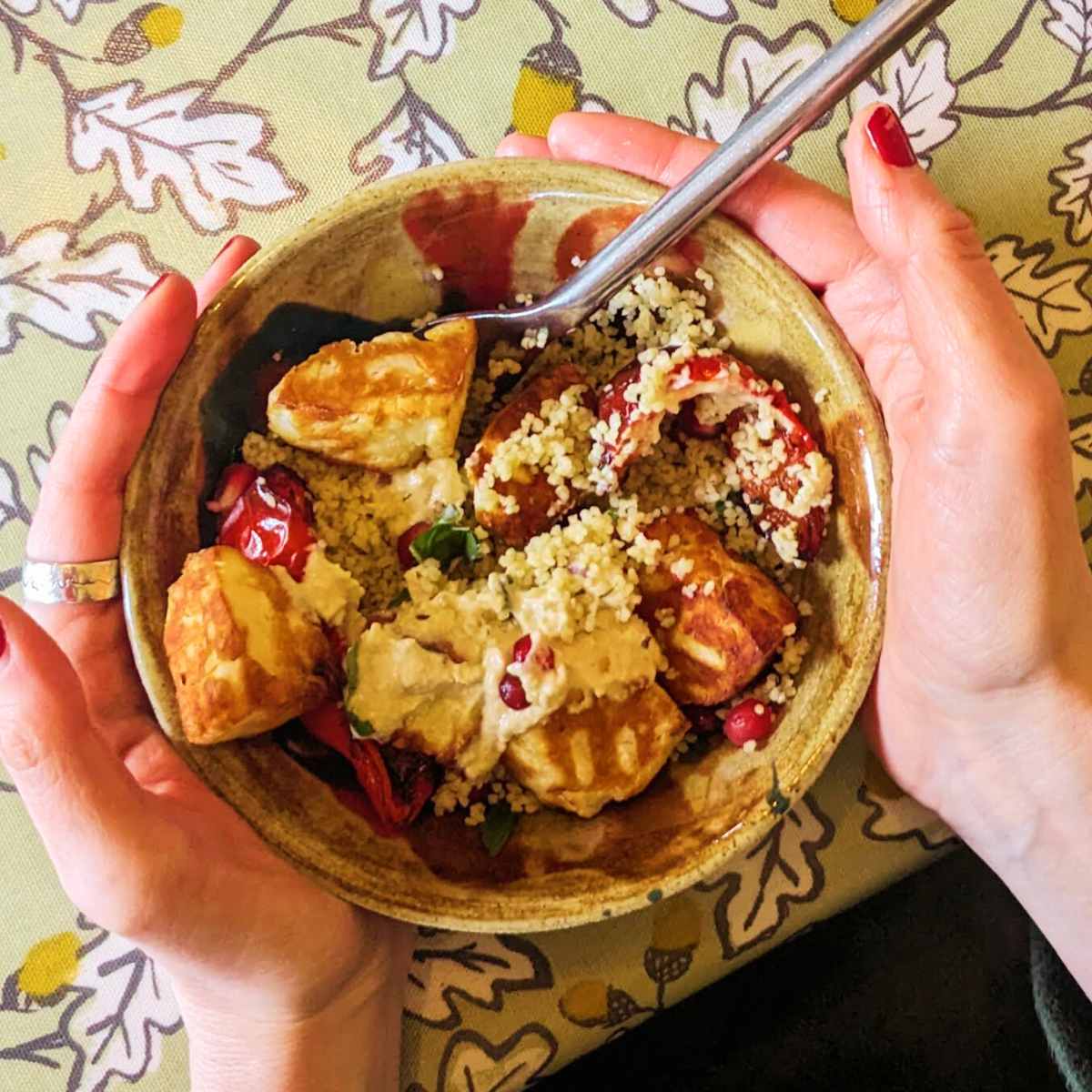 Two hands holding a bowl of halloumi and couscous salad