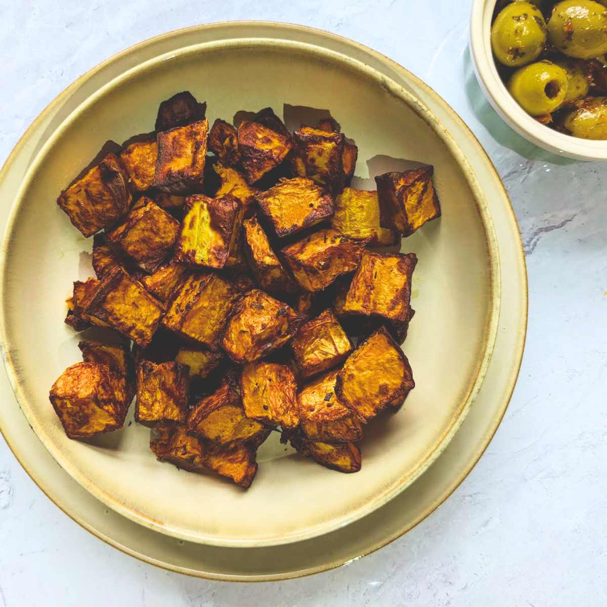 A bowl of cubed and roasted butternut squash with a small bowl of olives by the side