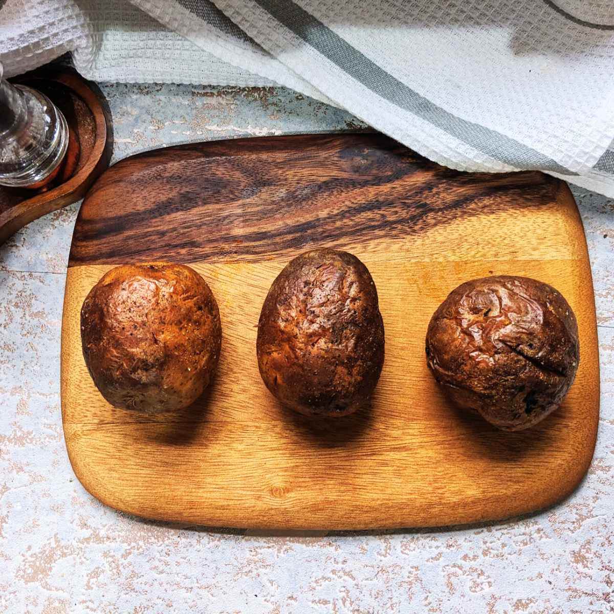Three baked potatoes that have been cooked in air fryer sit on a wooden board.