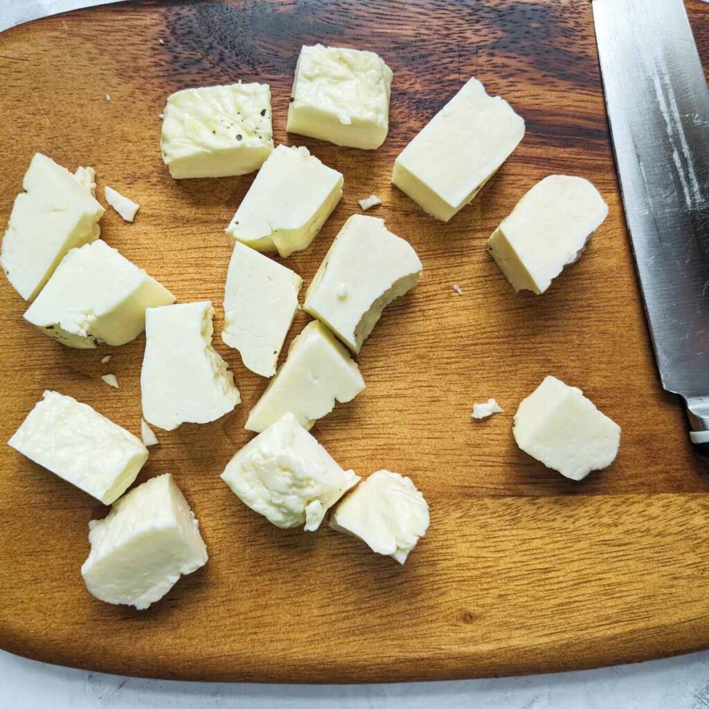 Raw cubed halloumi on a chopping board with a knife
