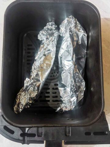 Two foil parcels in an air fryer basket.