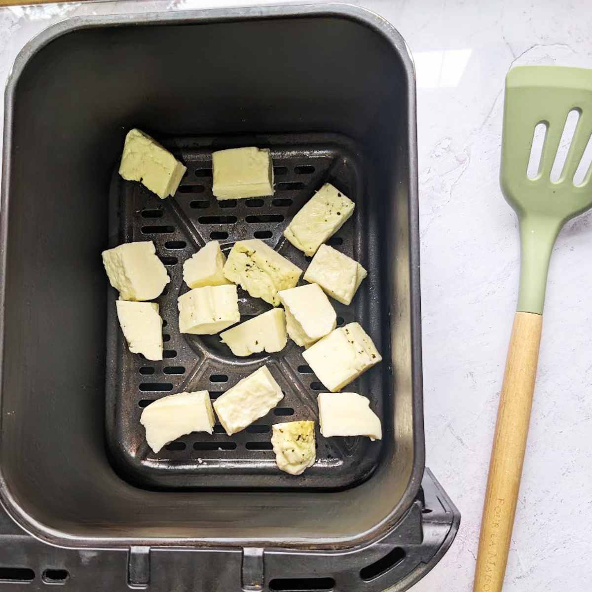 Uncooked cubed halloumi cheese in an air fryer basket