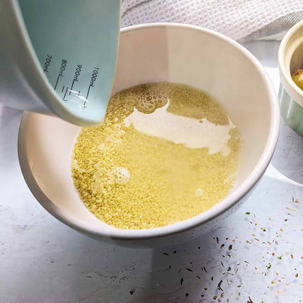 A measuring jug pouring water onto a bowl of dried couscous
