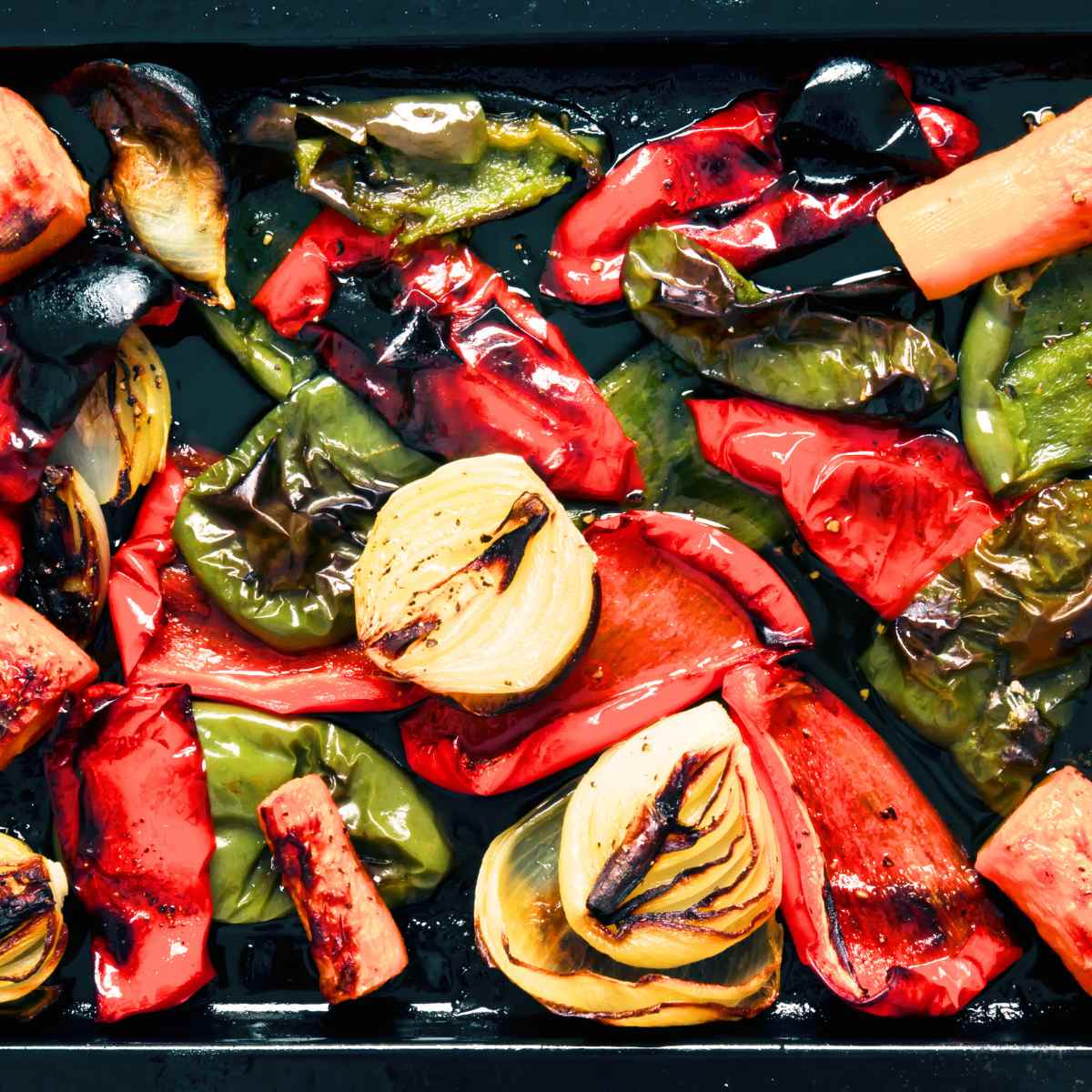 Chopped roasted peppers and onions in a baking tray.