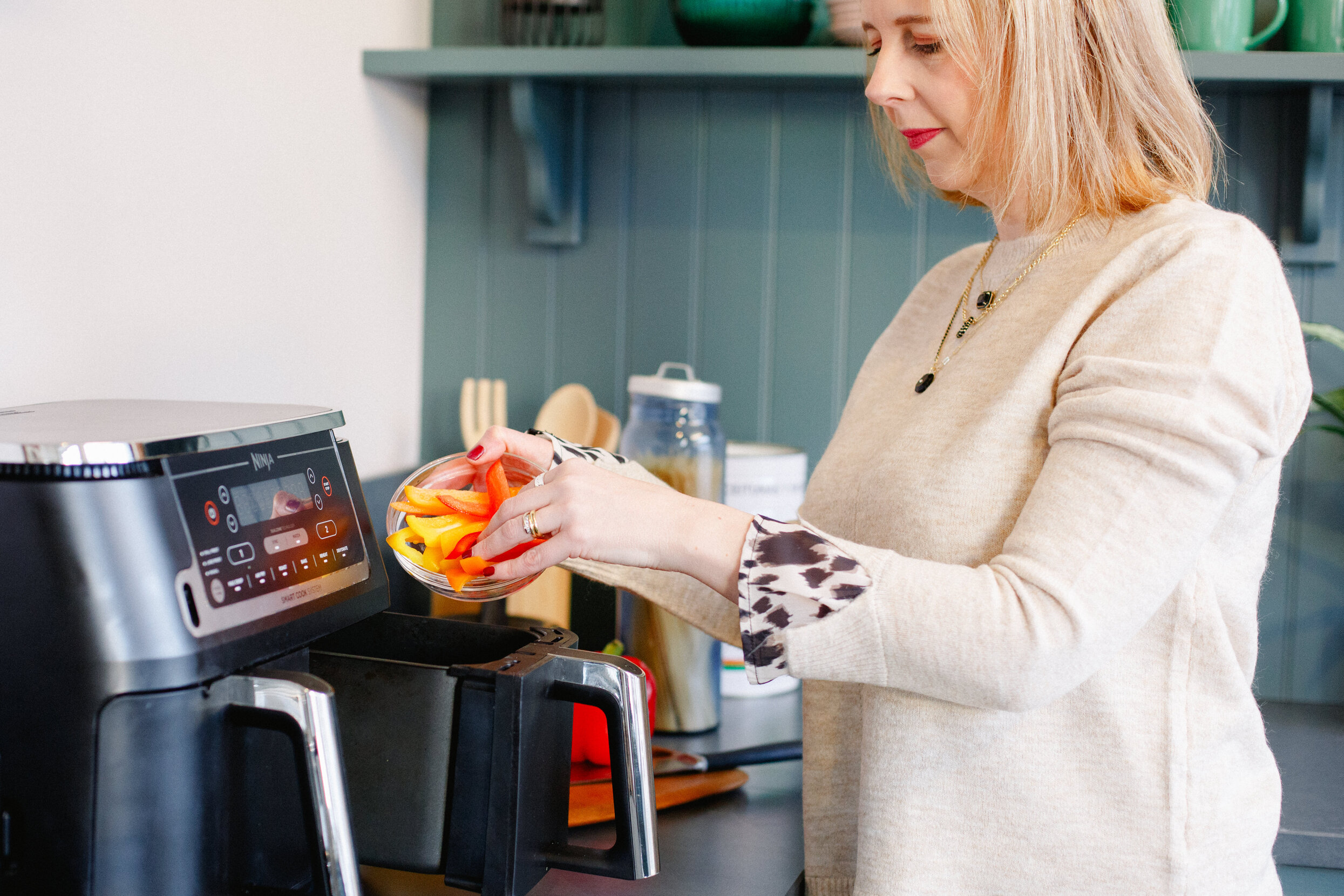 Jen from Start to Airfry putting chopped peppers into a Ninja air fryer drawer.