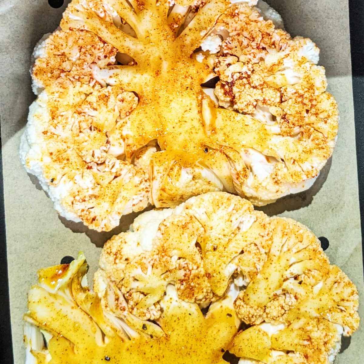 Two seasoned cauliflower steaks sit next to each other in an air fryer basket.