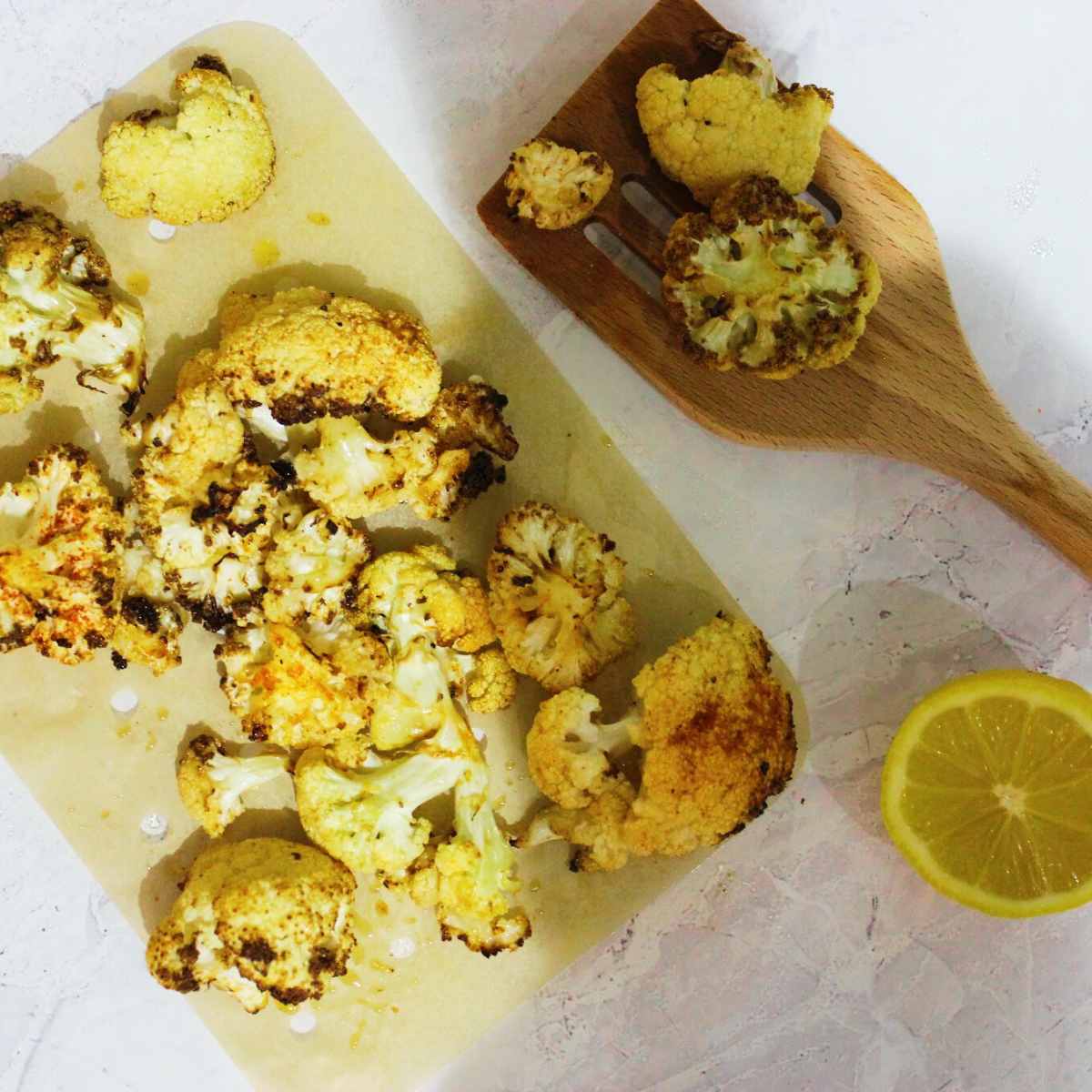 Roasted cauliflower that has been cooked in air fryer with cripsy edges sits on an air fryer liner with a lemon half by the side.