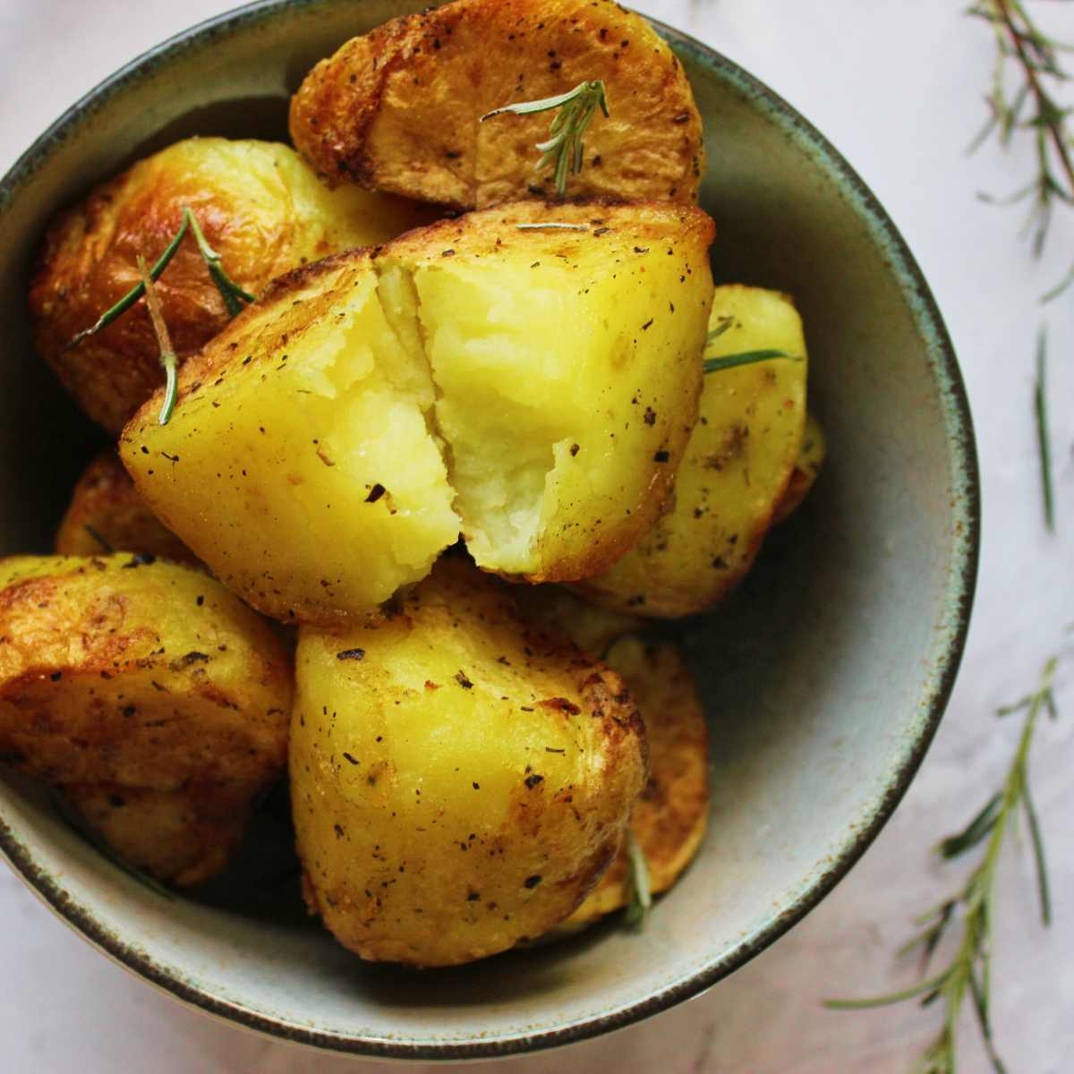Roast potatoes in a bowl with sprigs of rosemary alongside.