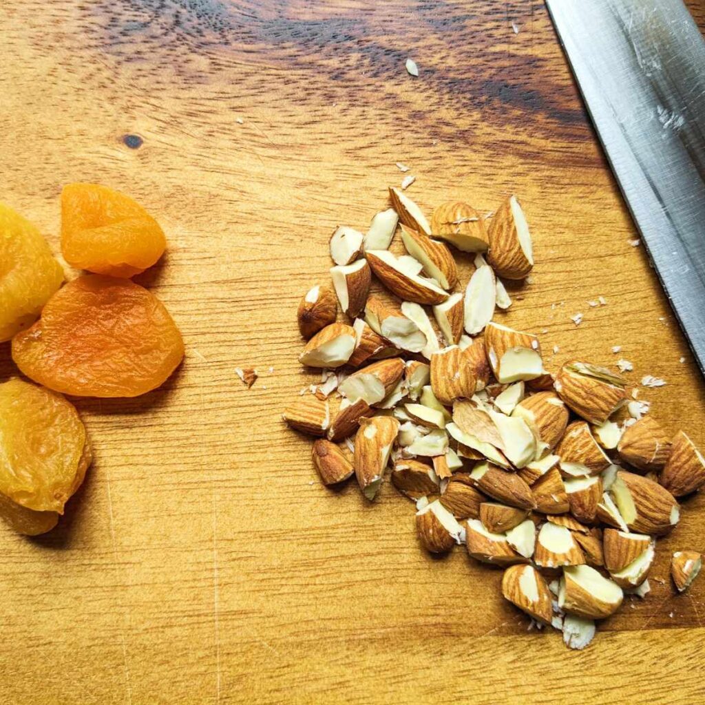 Chopped almonds on a board with apricots.