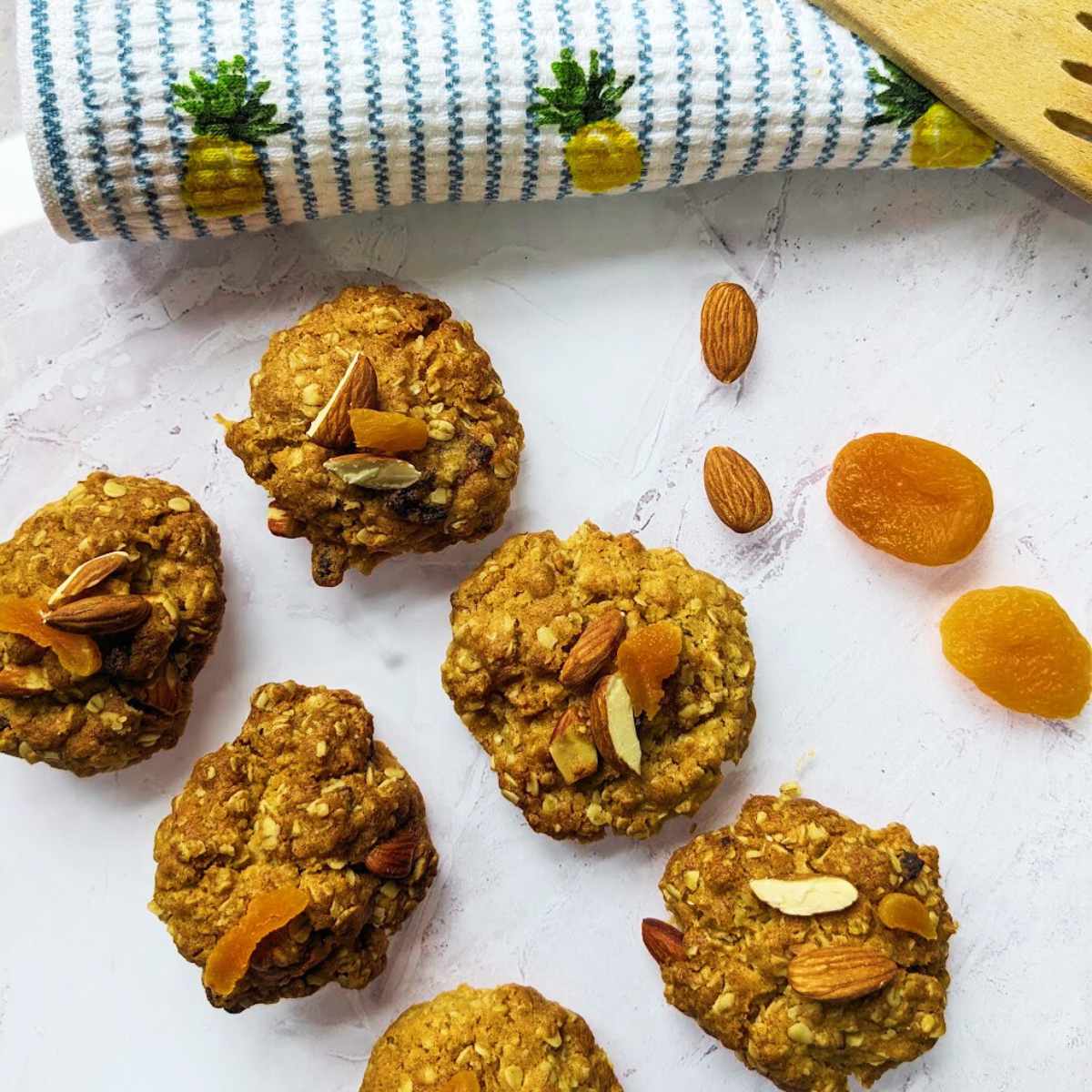 Six oat cookies on a board with apricots and almonds