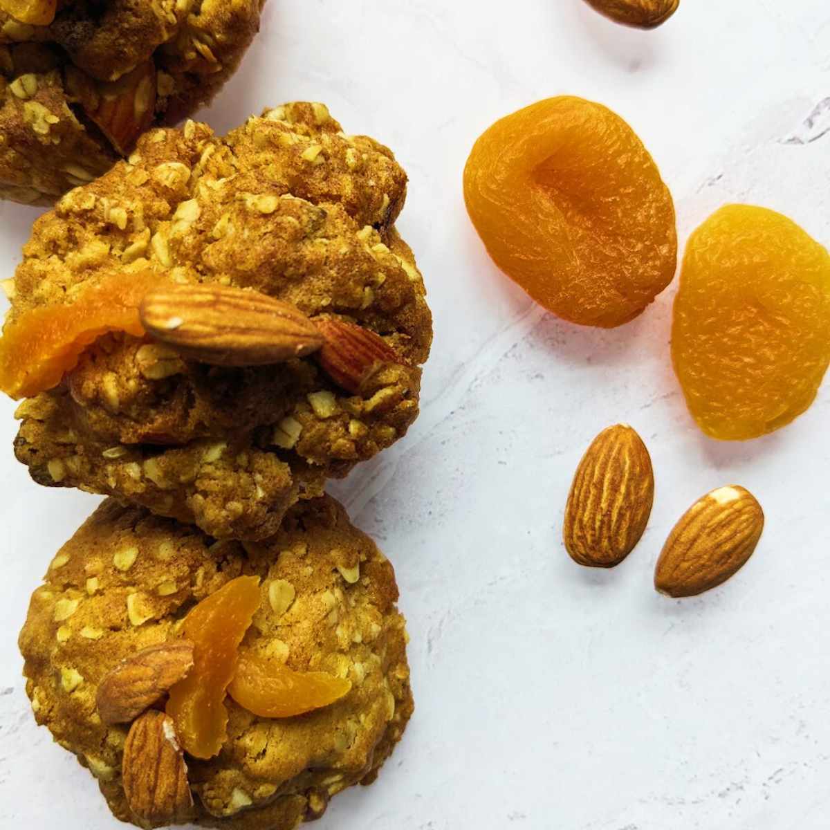 Three oat cookies on a board with apricots and almonds