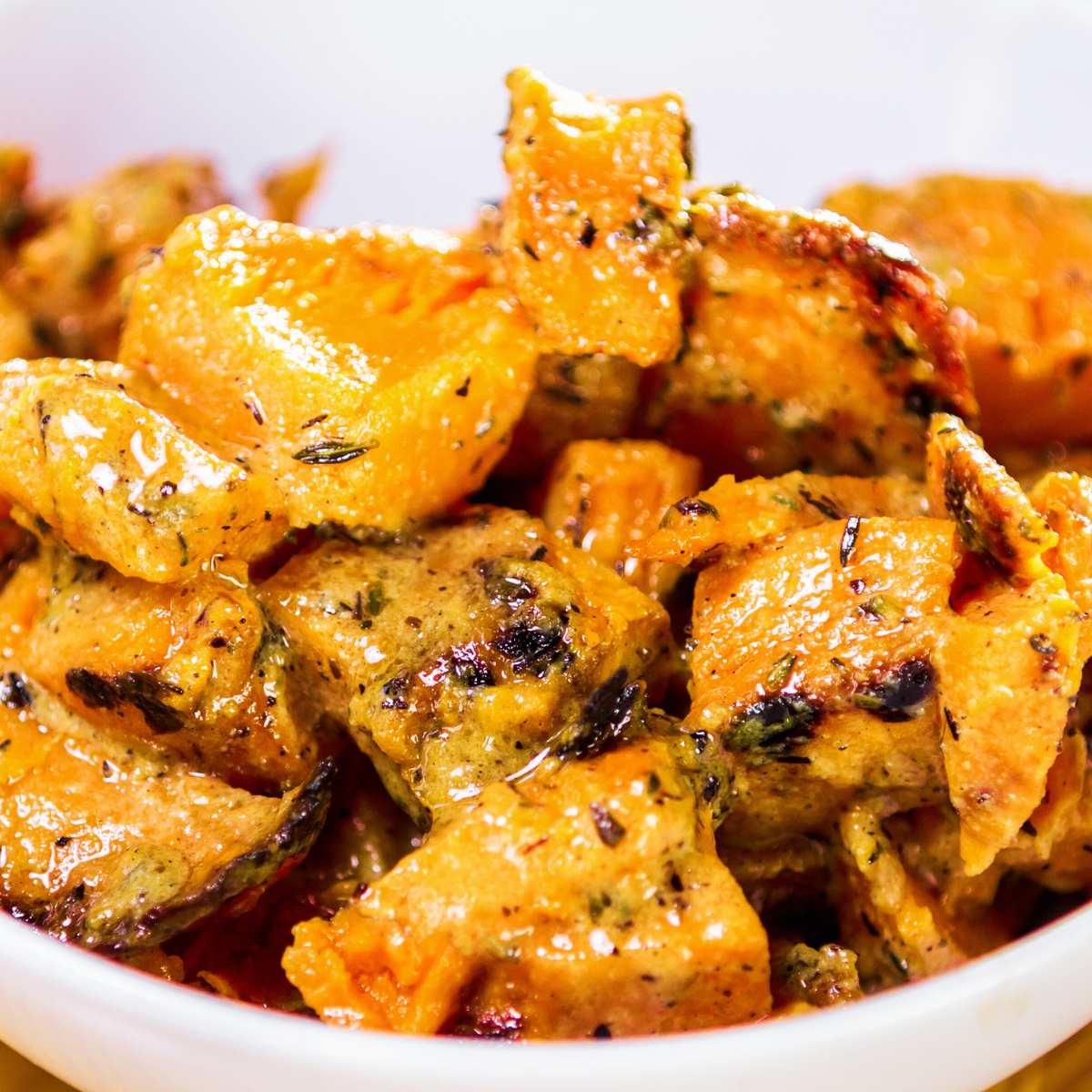 A bowl of roasted butternut squash topped with herbs.
