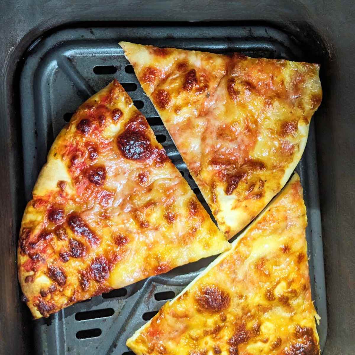 Three slices of pizza in an air fryer basket.