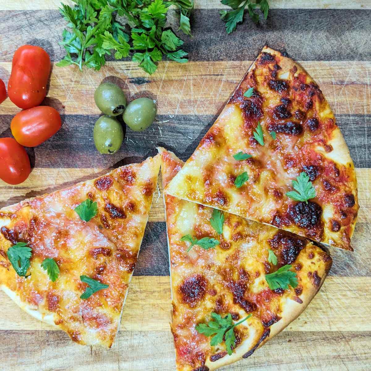 Slices of pizza on a chopping board with olives and tomatoes at the side.