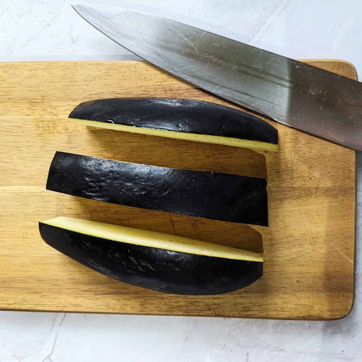 Aubergine slices on a chopping board with a knife.