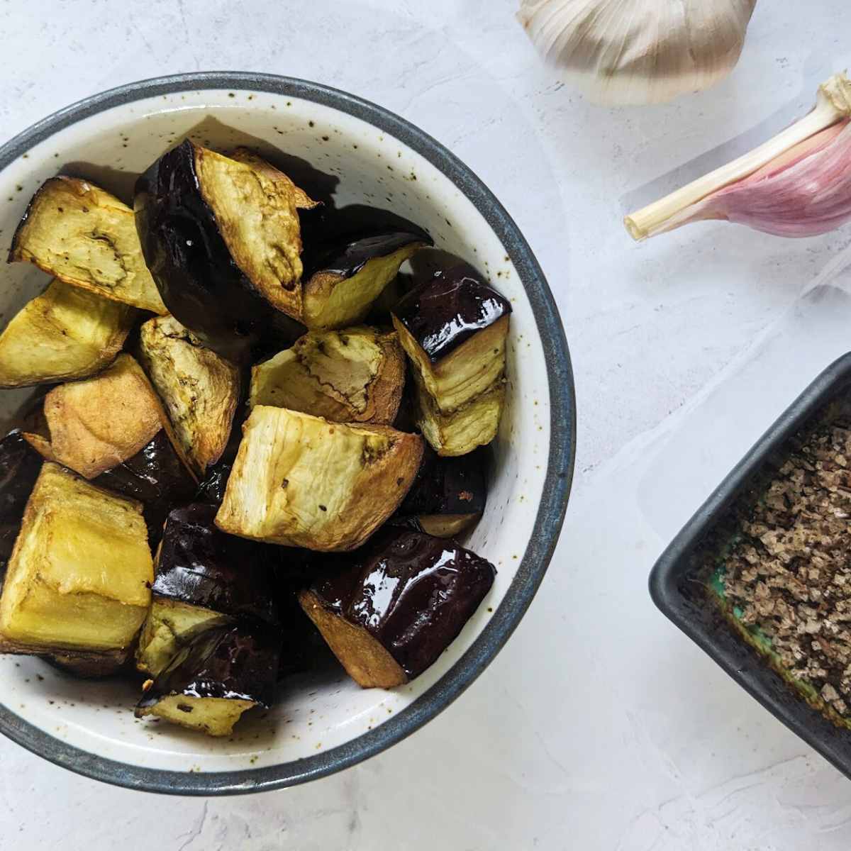A bowl of cooked aubergine pieces with garlic and salt at the side.