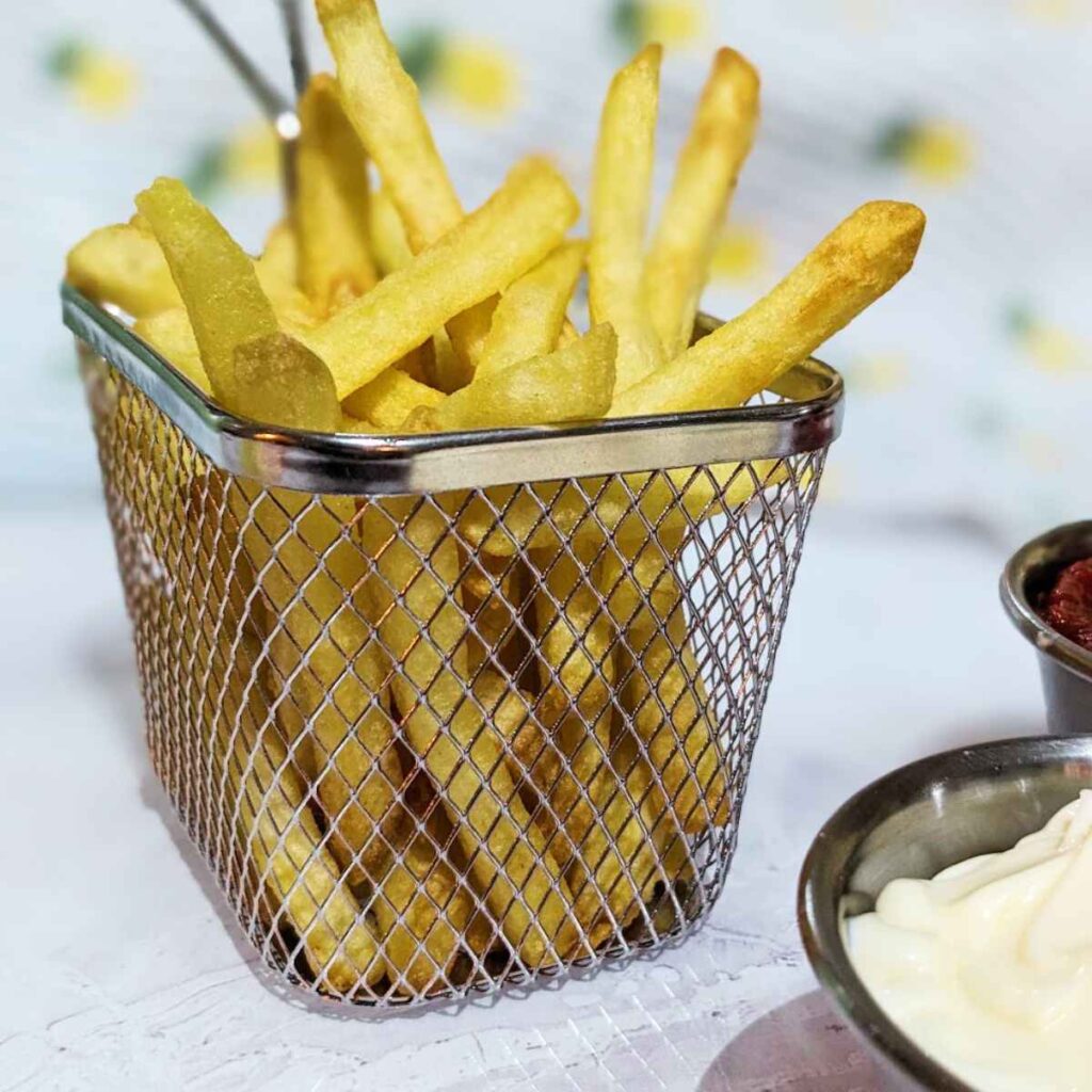 Cooked French Fries in a wire serving basket with a serving of mayo at the side