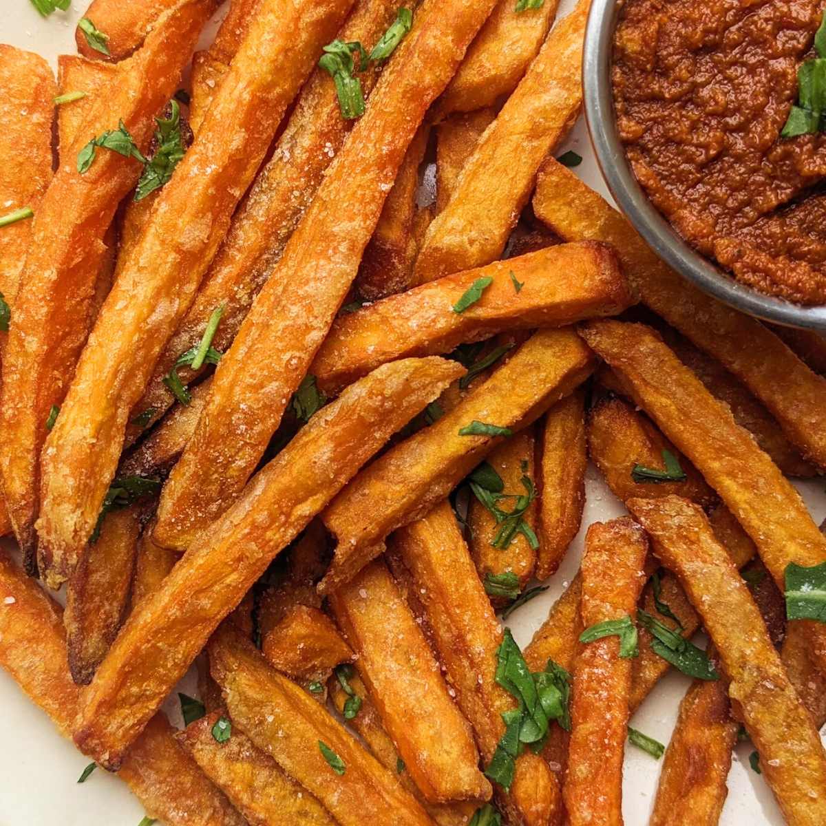 A plate of sweet potato fries with a tomato dipping sauce at the side.
