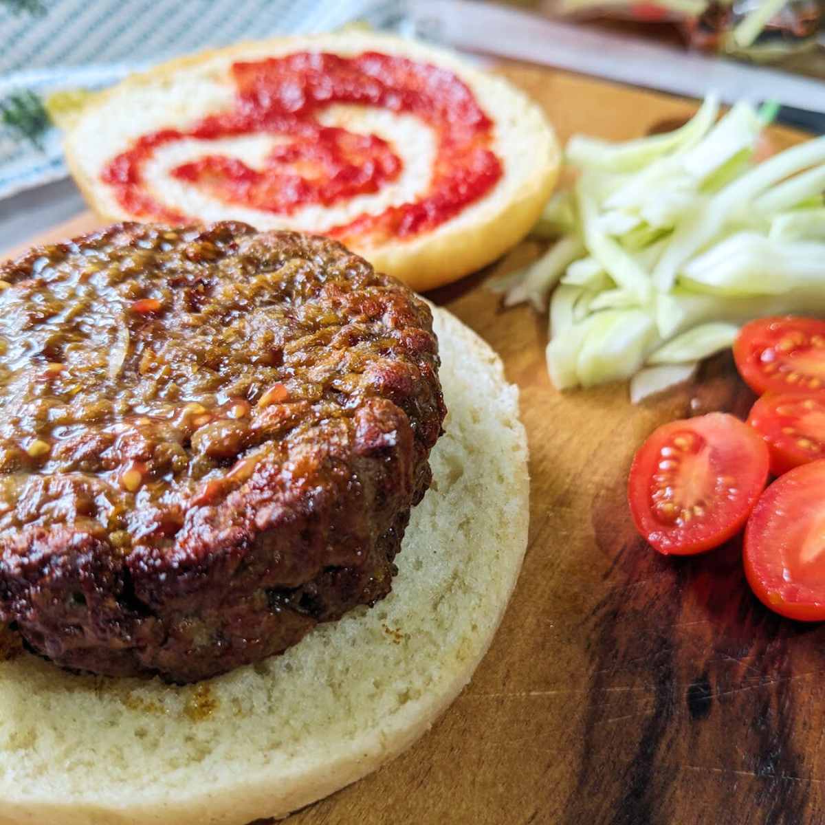 A cooked burger patty sits on a burger bun with a swirl of ketchup and salad ingredients.