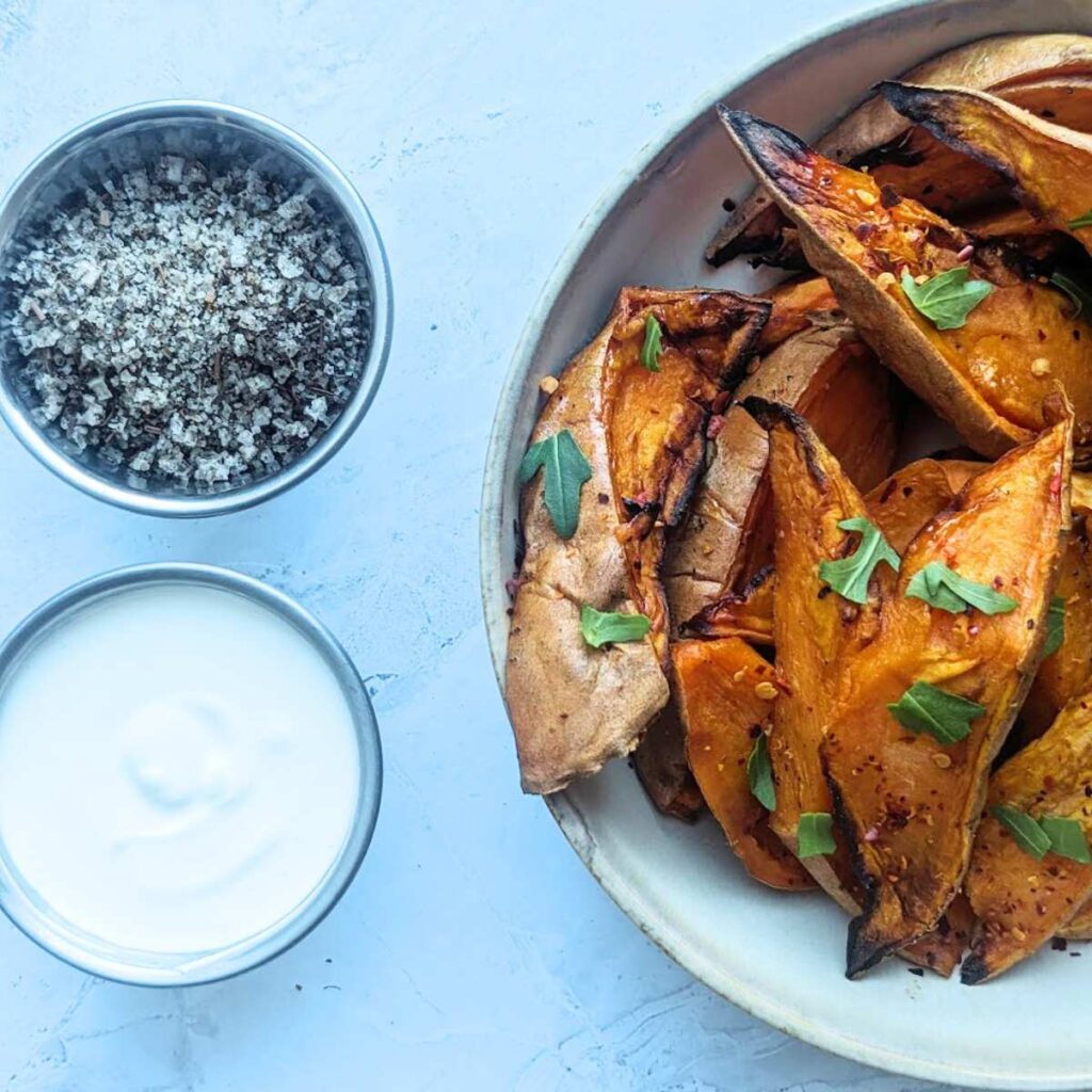 A bowl of sweet potato wedges with seasoning and a creamy dip at the side.