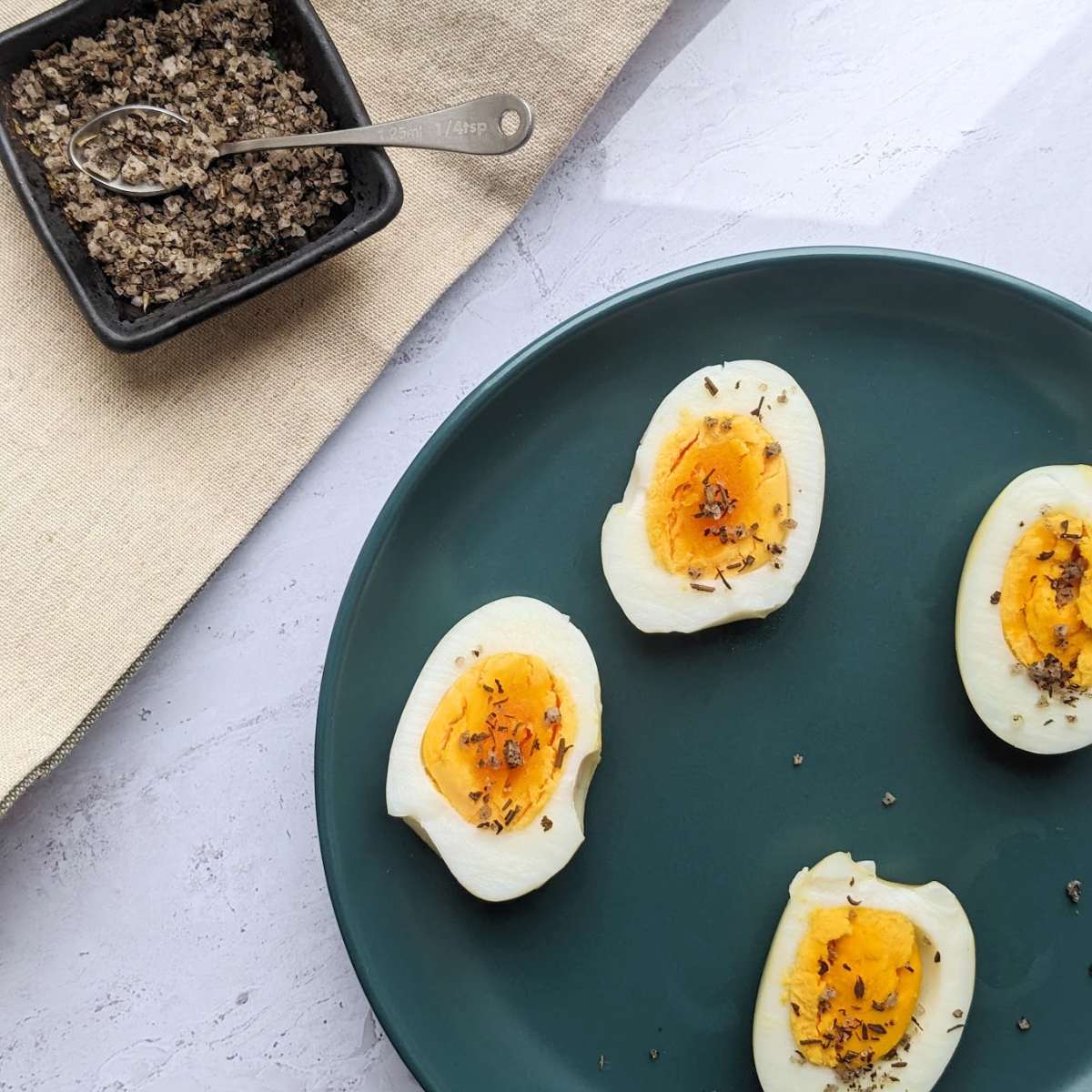 Halved boiled eggs on a blue plate, topped with a sprinkle of salt and pepper.