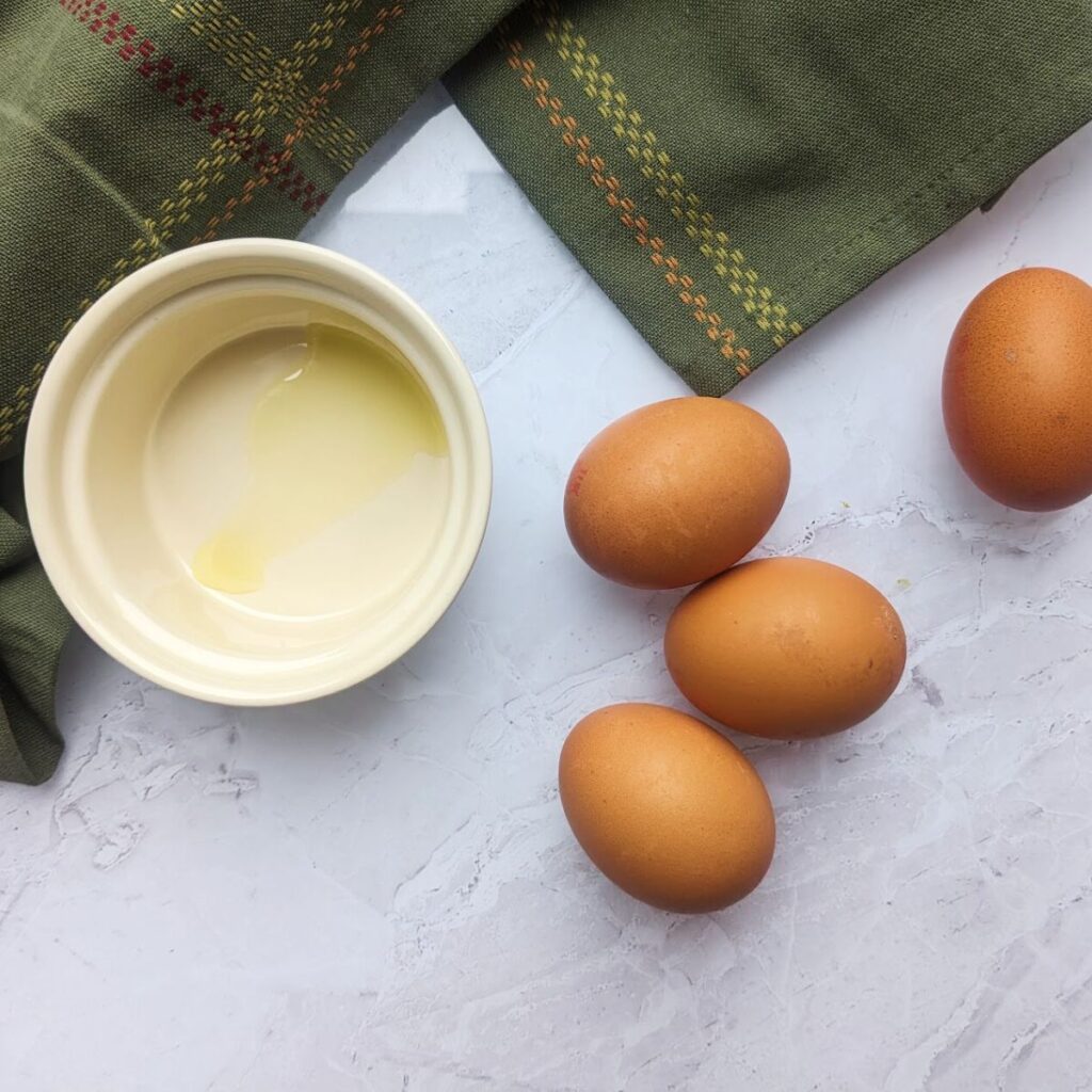 Whole eggs on a kitchen worktop next to an oiled ramekin.