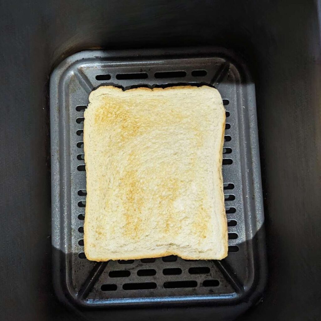 A slice of toasted bread in an air fryer basket.