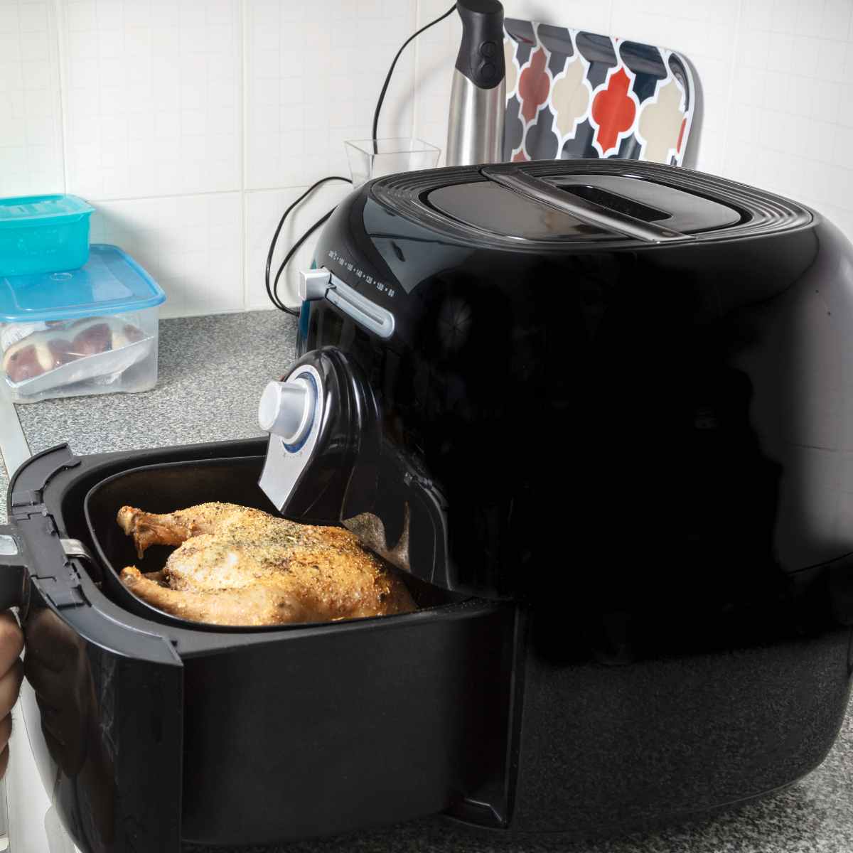 Air fryer on kitchen counter with a whole chicken in the open basket.