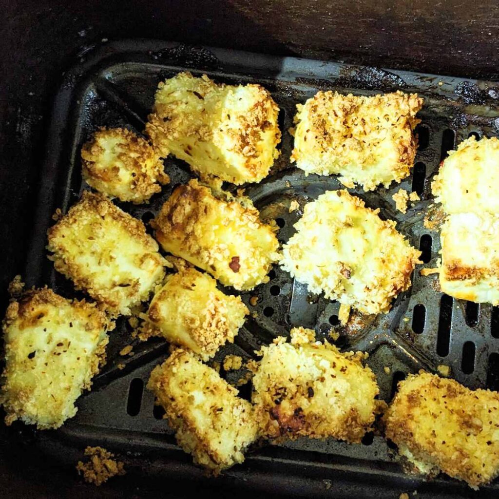 Halloumi pieces cooking in an air fryer basket.