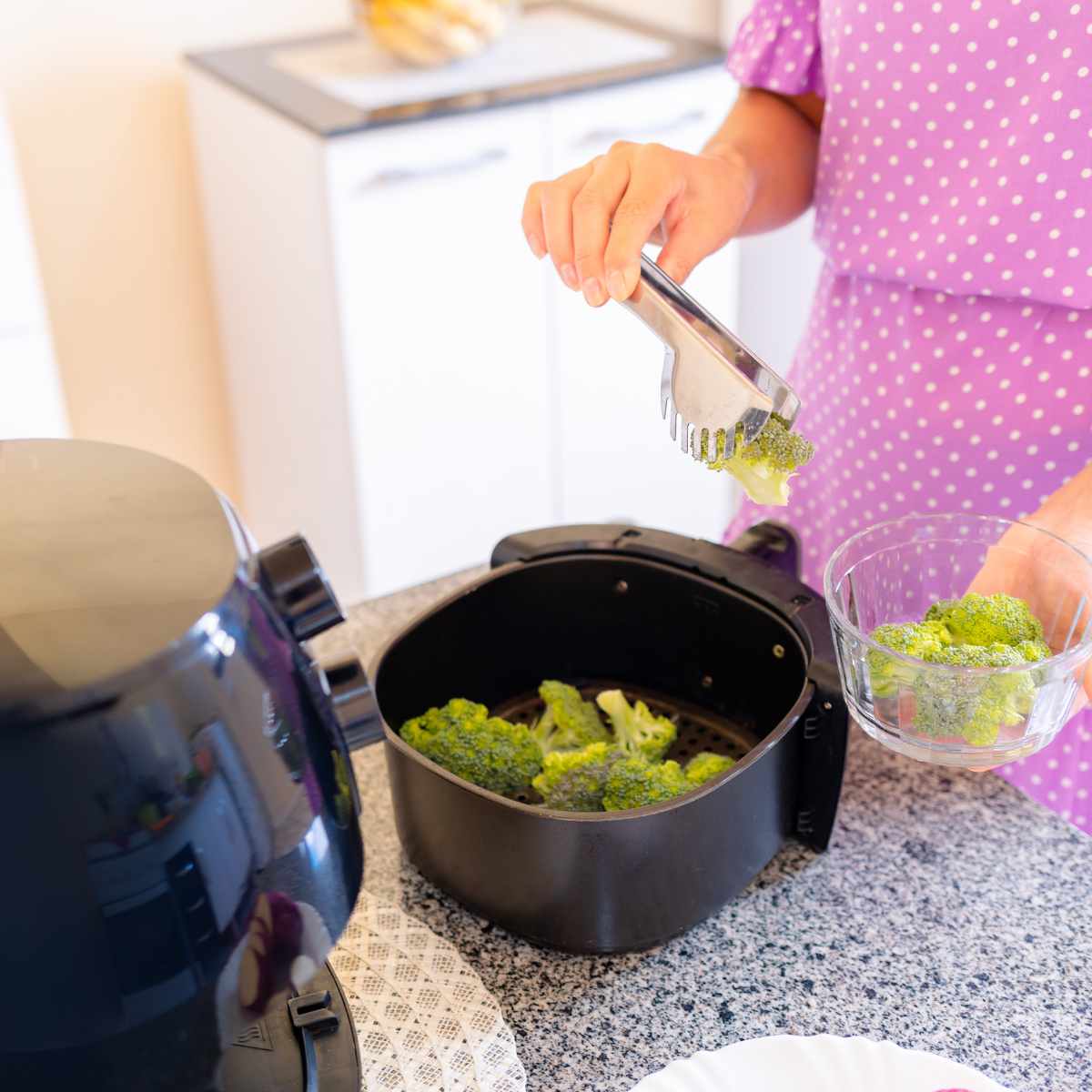 A lady is placing broccoli into an air fryer basket.