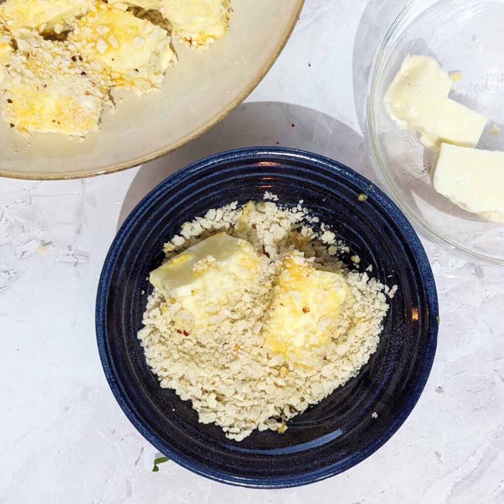 Halloumi pieces being coated in panko breadcrumbs in a bowl.