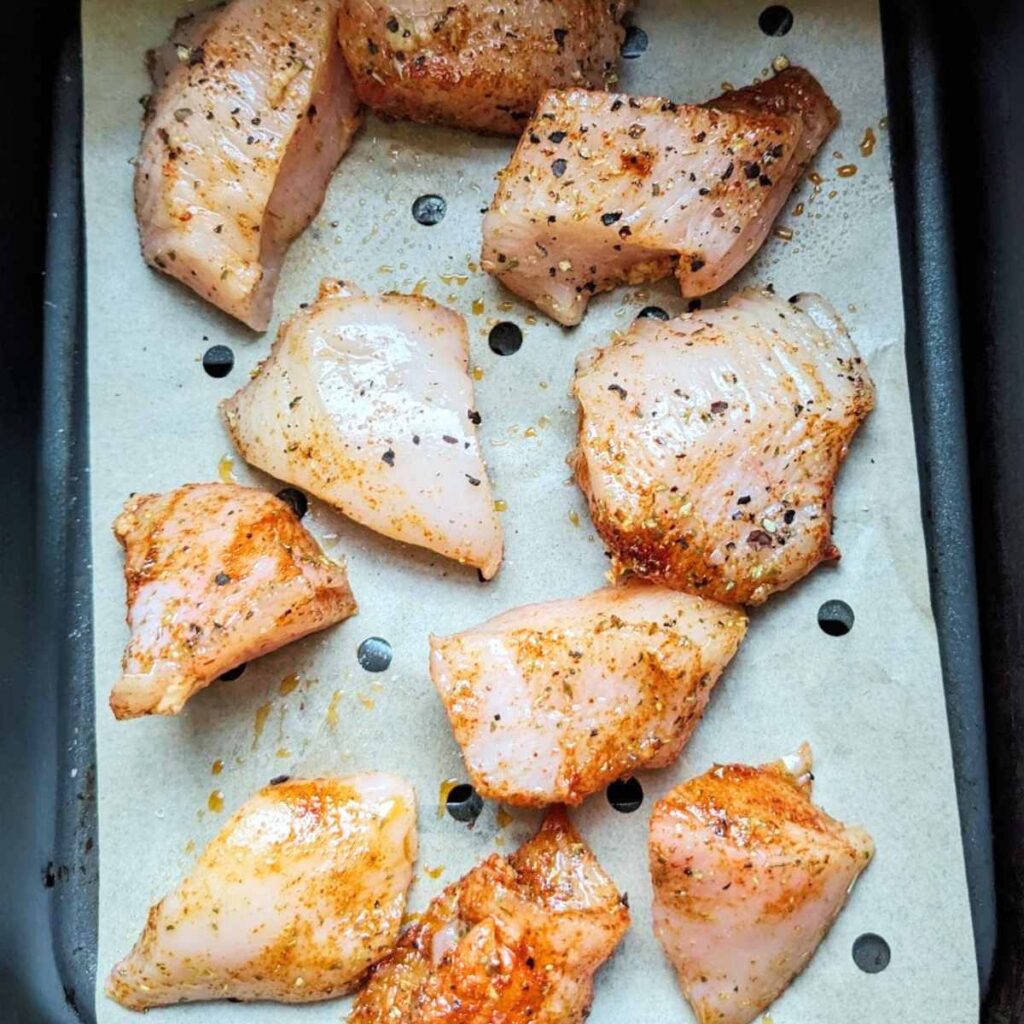 Diced chicken breast on parchment paper inside an air fryer basket.