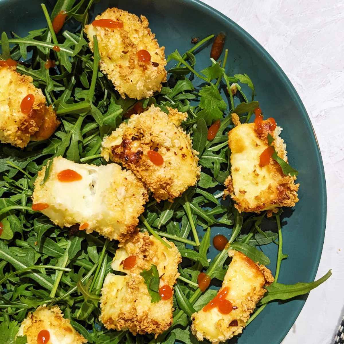 Air-fried halloumi bites on a bed of rocket with chili sauce drizzled on top.