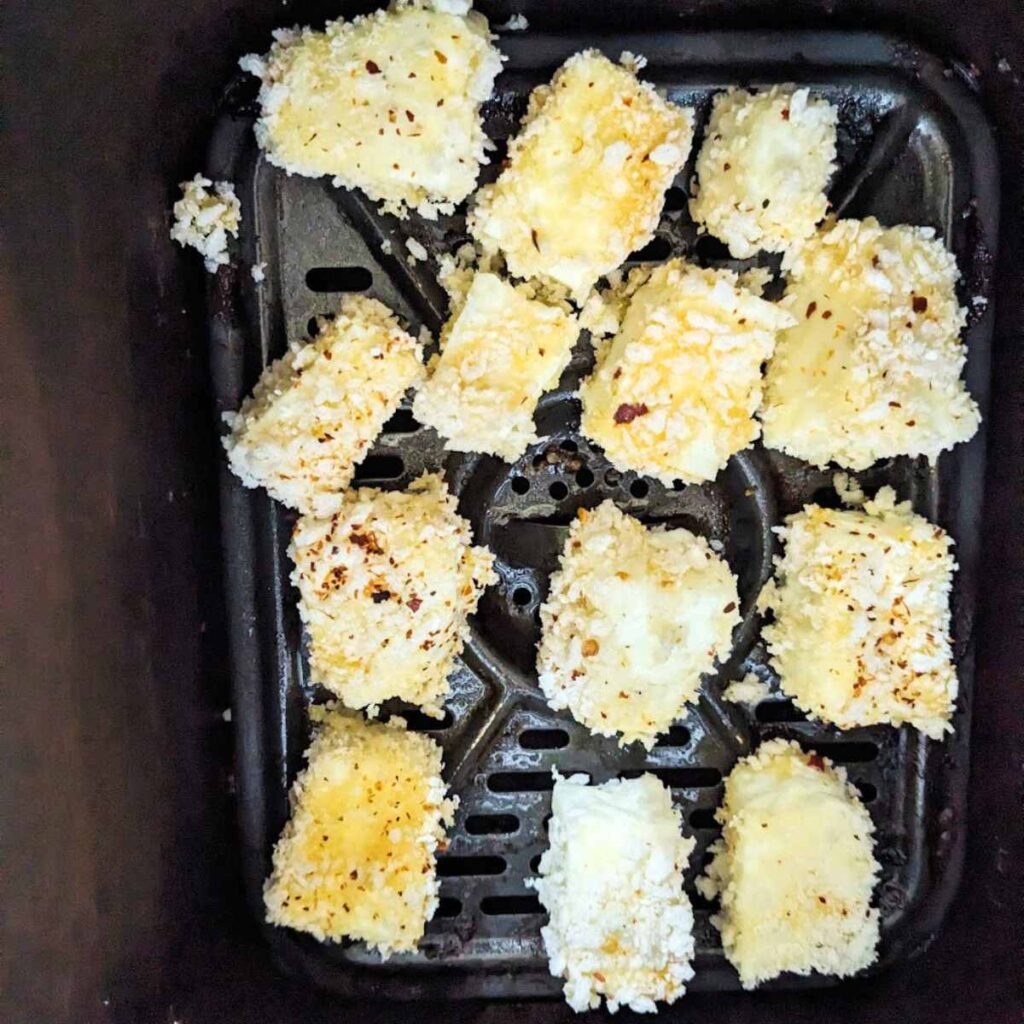 Pieces of halloumi coated in panko breadcrumbs in an air fryer basket.