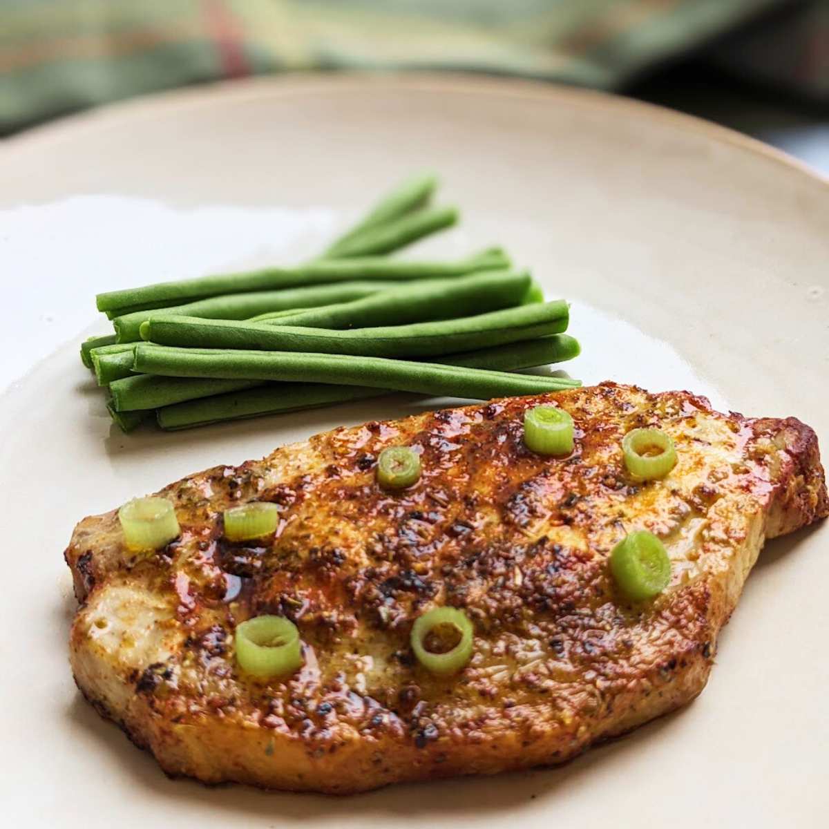 An air fried pork steak on a plate with green beans at the side.