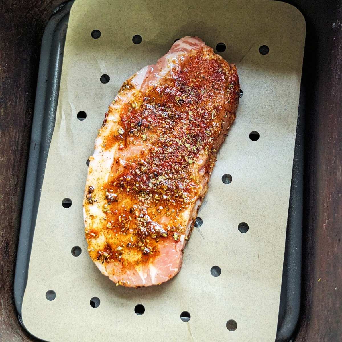 A pork steak on a liner in an air fryer basket.