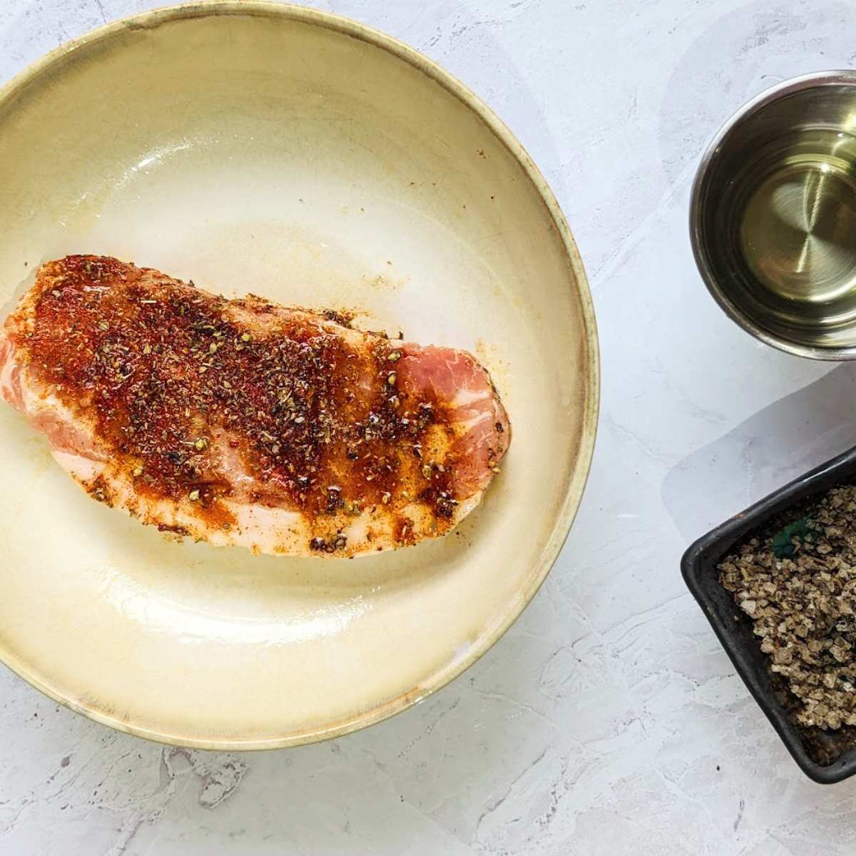 A pork steak covered in a herby rub on a plate.