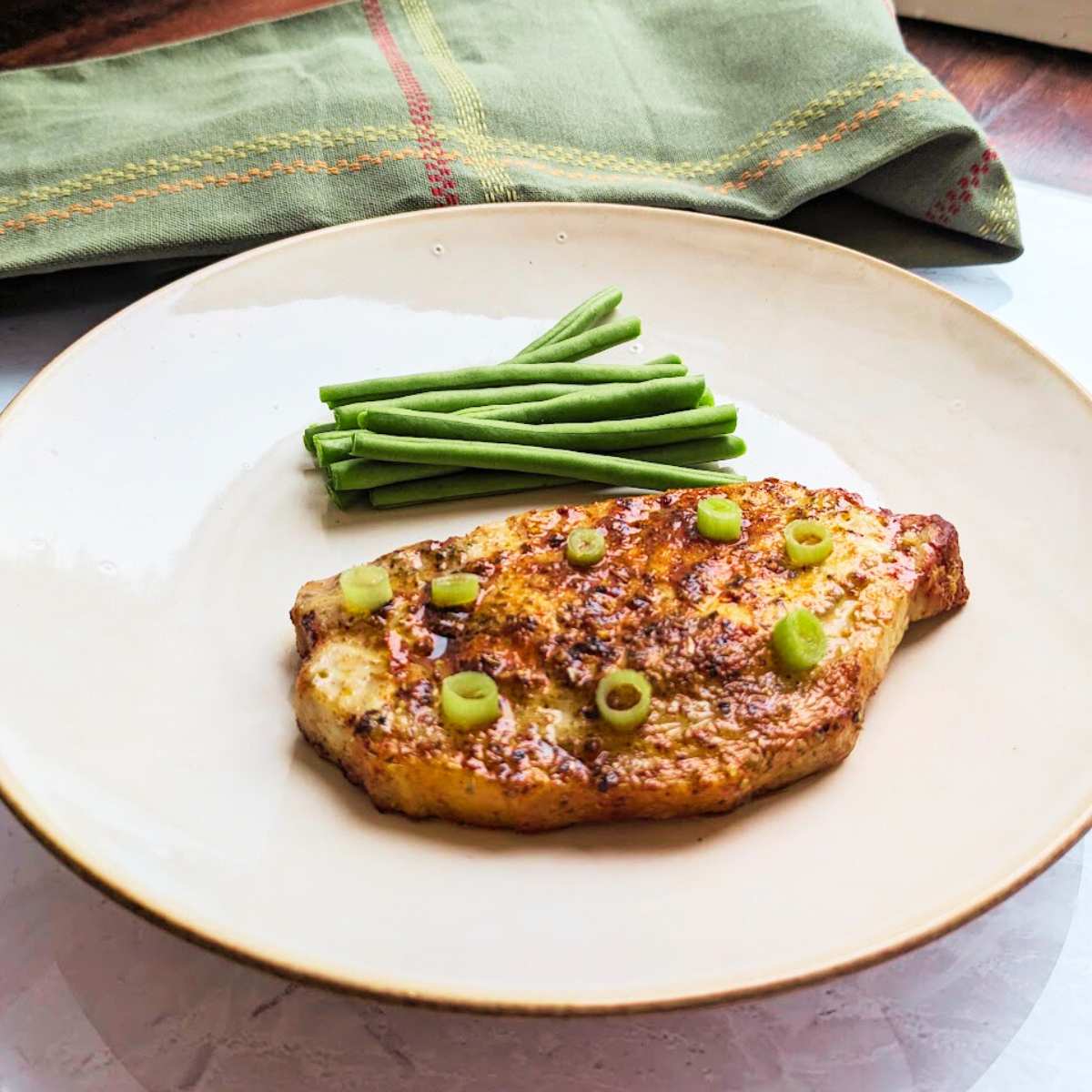 A pork steak served on a plate with a side serving of green beans.