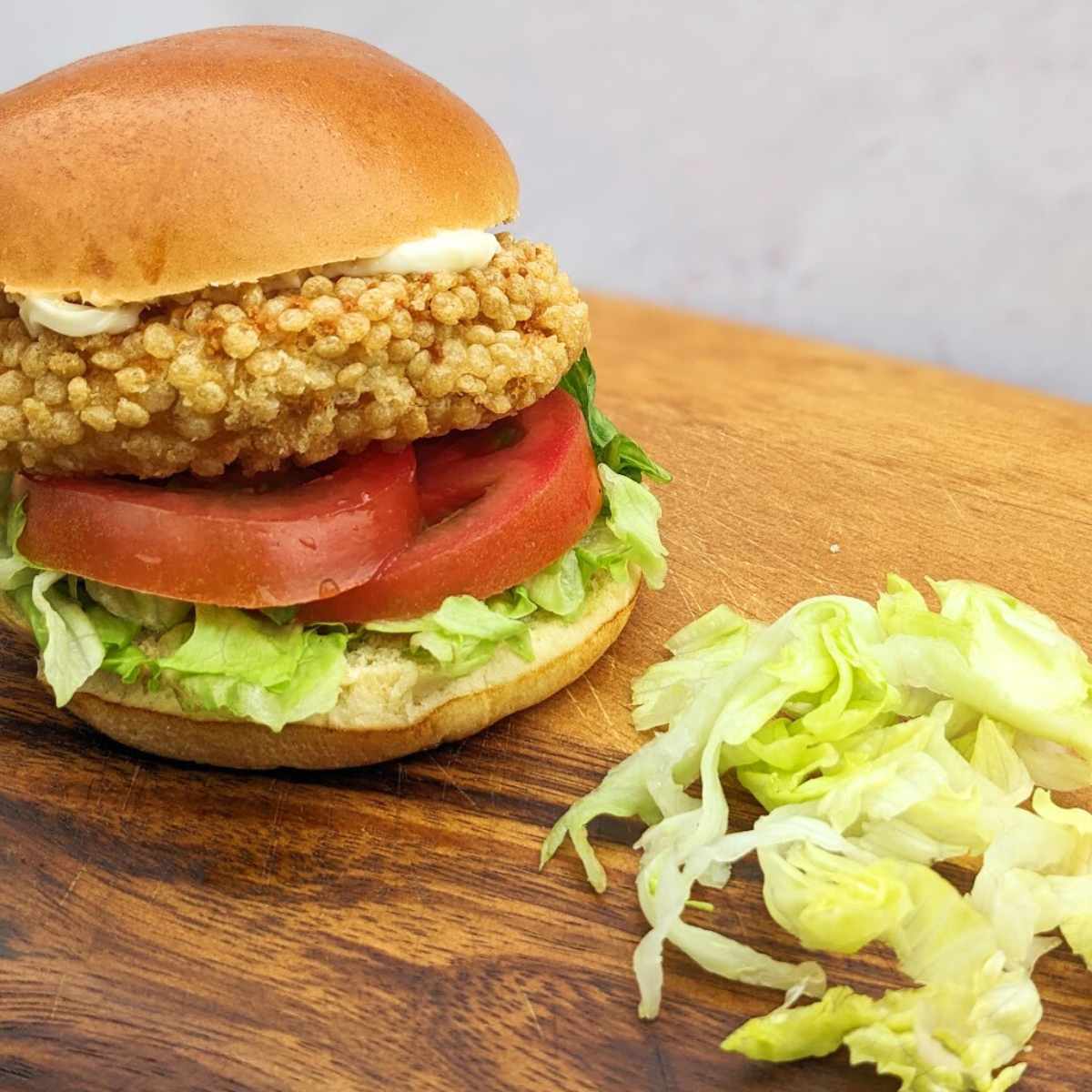 A chicken patty in a bun with salad on a wooden chopping board
