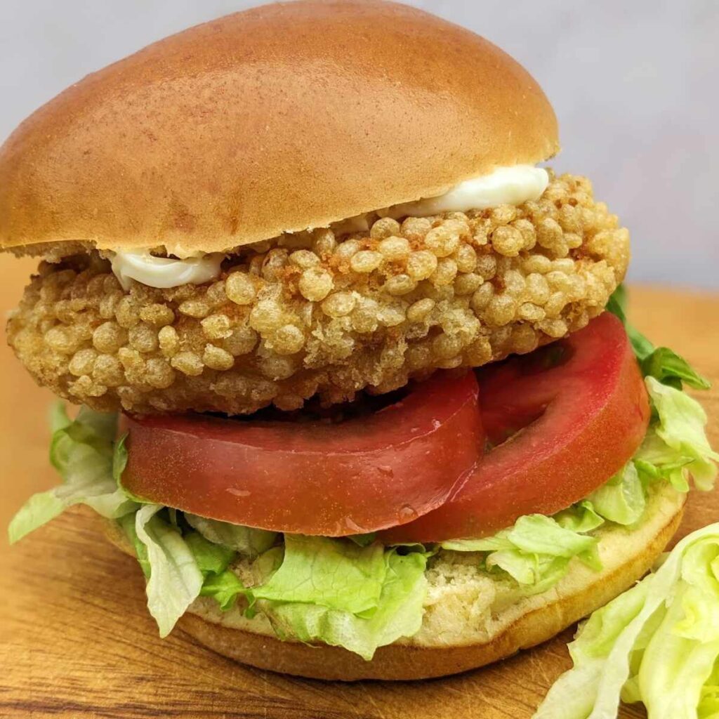 A chicken patty in a bun with salad and mayo, sitting on a kitchen board.