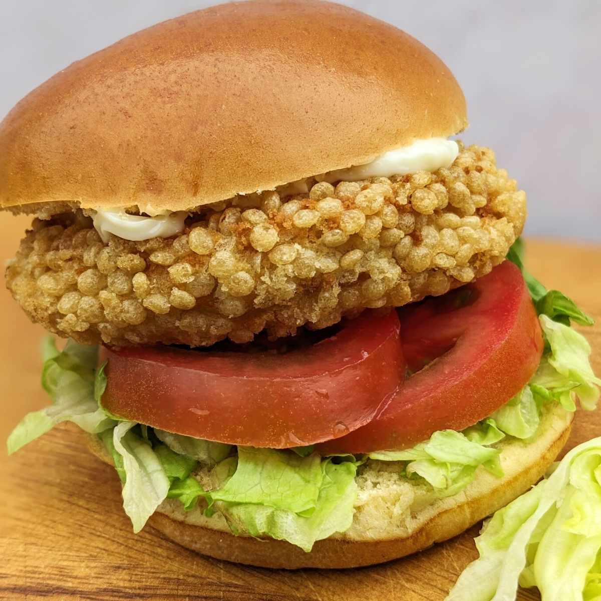 A chicken patty in a bun with salad and mayo, sitting on a kitchen board.