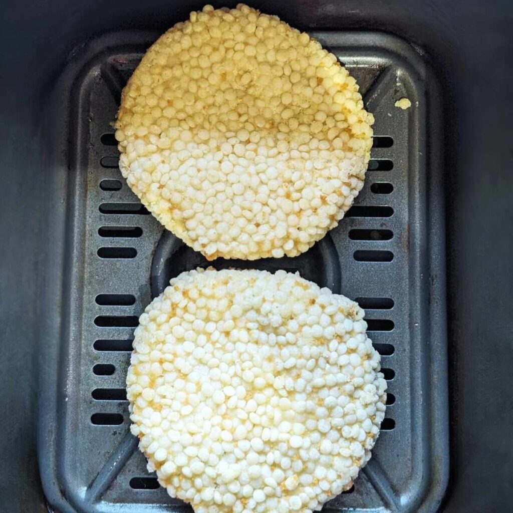 Two frozen chicken patties in an air fryer basket.