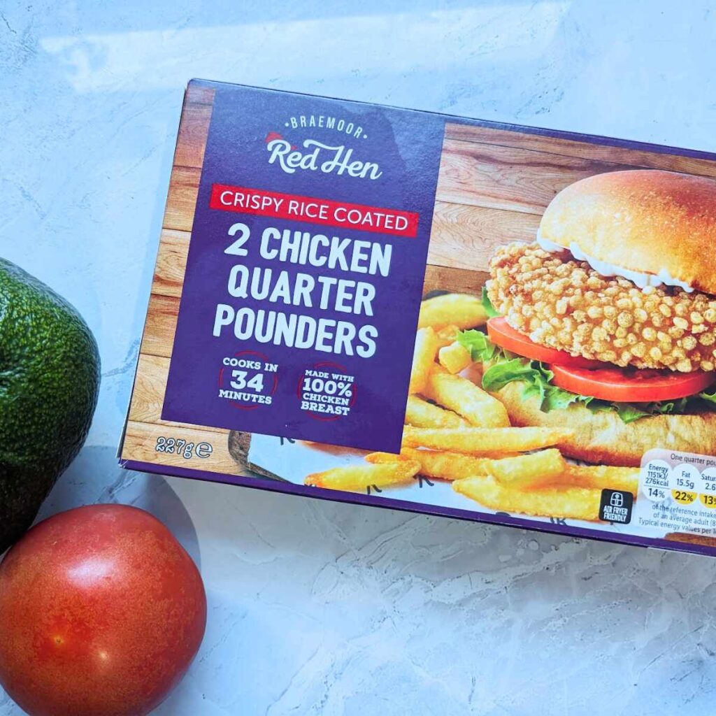 A box of frozen chicken patties next to an avocado and a tomato.