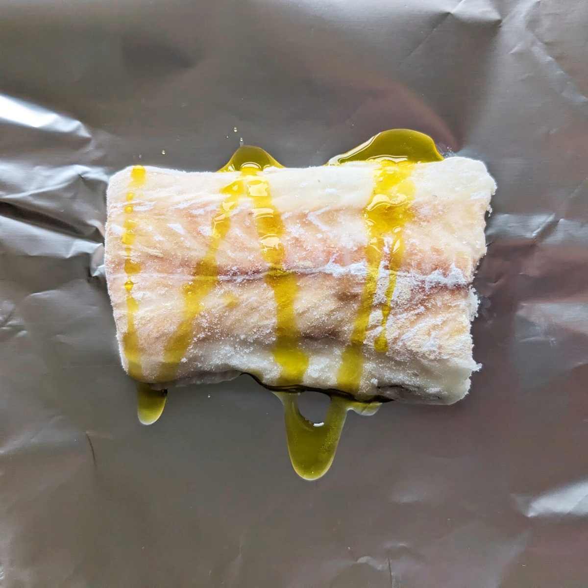 A haddock fillet drizzled with oil on a piece of aluminum foil.