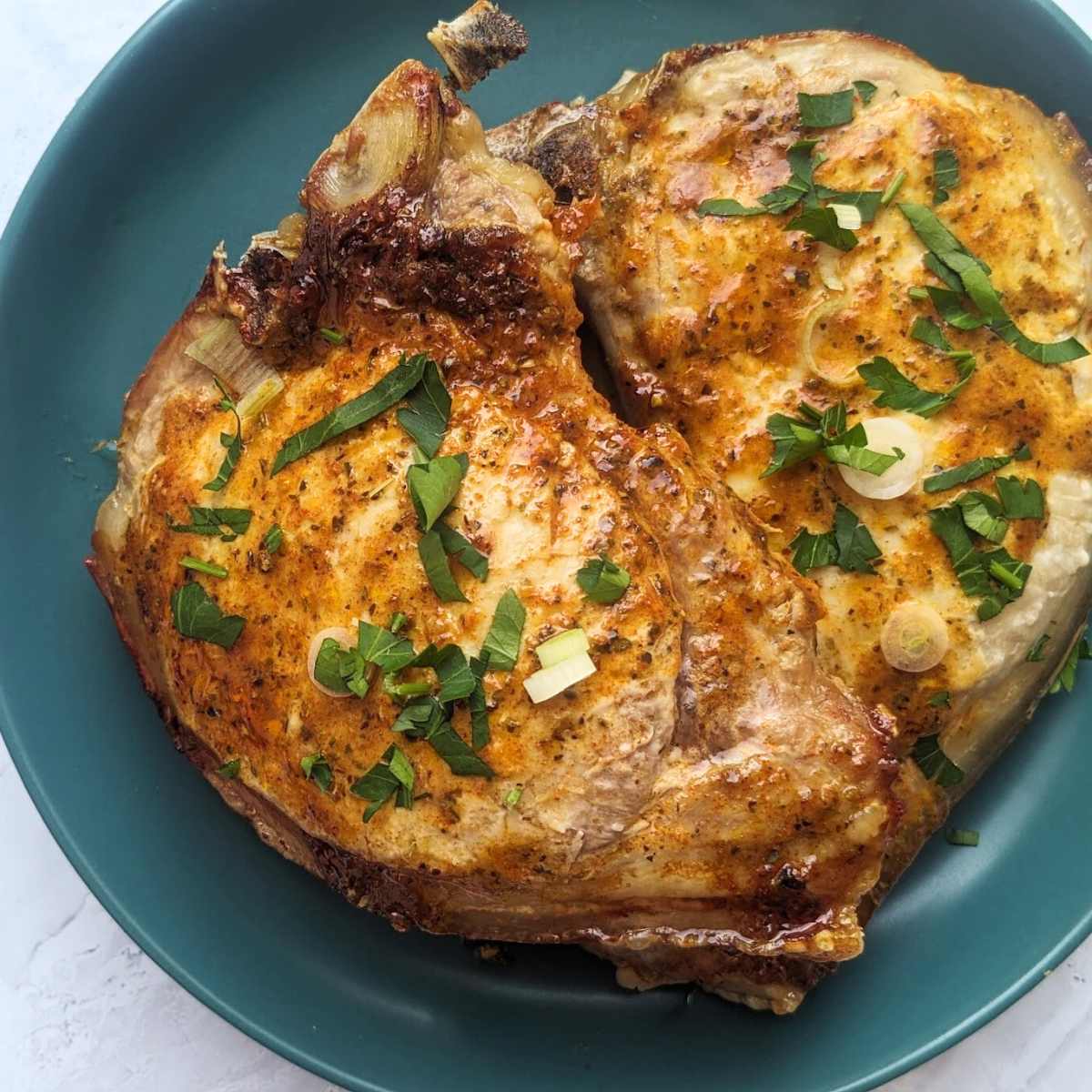 Two air fryer bone-in pork chops on a blue plate.
