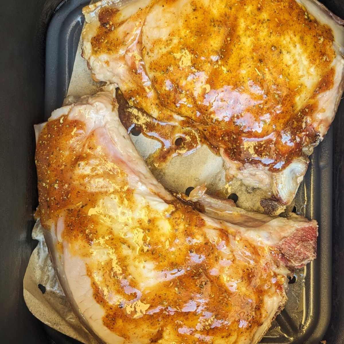 Two pork chops in an air fryer basket.