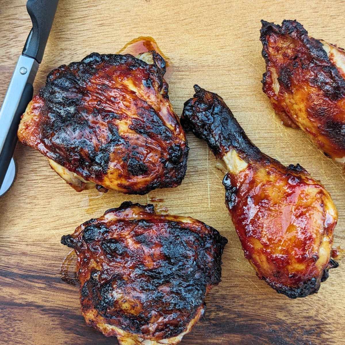 Chicken drumsticks and thighs after cooking in an air fryer. They sit on a board with silicone tongs at the side.